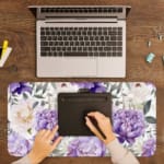 Infidu desk pad with colorful floral design on white background. Features large yellow and purple flowers with green and grayish leaves. A writing pad on top of the desk pad