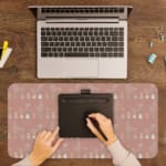 Infidu Beige Desk Mat with a subtle pattern of small shapes or icons on a soft beige background. A writing pad on top of the desk pad