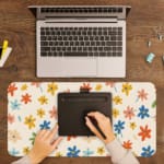 Infidu Colorful Floral Design Desk Pad with vibrant flowers in yellow, pink, blue, orange, and green on a light pink background. A writing pad on top of the desk pad