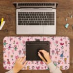 Infidu desk pad with playful floral and figures design on a light pink background, featuring colorful flowers and figures. A writing pad on top of the desk pad