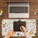 Infidu desk pad with soft pastel floral design on a light pink background, featuring delicate light blue, pink, and beige flowers. A writing pad on top of the desk pad