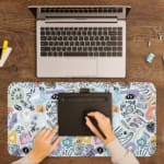 Infidu desk pad with pastel abstract shapes and symbols on a pale blue background. A writing pad on top of the desk pad