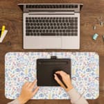 Infidu Playful Abstract Shapes Desk Pad featuring colorful eyes, symbols, and shapes on a light background. A writing pad on top of the desk pad