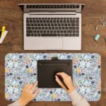 Desk pad with colorful abstract shapes in orange, black, white, and blue on a light blue background. A writing pad on top of the desk pad