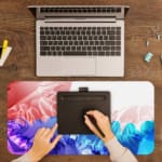 Desk pad with a gradient color design transitioning from red to blue and green, featuring abstract wavy patterns. A writing pad on top of the desk pad