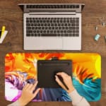 Desk pad with a vibrant abstract swirl design in orange, yellow, gray, blue, and pink. A writing pad on top of the desk pad