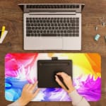Infidu Vibrant Watercolor Design Desk Pad with abstract, colorful swirls of pink, orange, yellow, blue, and purple. A writing pad on top of the desk pad