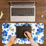 Desk pad with blue flowers, yellow centers, and green leaves on a white background. A writing pad on top of the desk pad