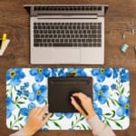 Desk pad with light blue flowers, yellow centers, and green leaves on a white background. A writing pad on top of the desk pad