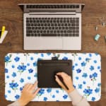 Desk pad with small blue flowers and dark green leaves on a white background. A writing pad on top of the desk pad