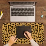 Infidu Leopard Print Desk Pad features a leopard print pattern with a tan background and black spots, resembling natural leopard fur. A writing pad on top of the desk pad