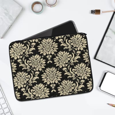 Laptop sleeve with a black background and detailed gold floral design, featuring secure zip closure. laptop sleeve kept on a plain white background