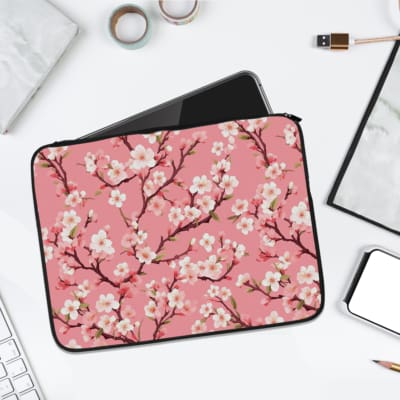 Pink laptop sleeve with a cherry blossom design featuring white flowers and brown branches on a pink background. laptop sleeve kept on a plain white background