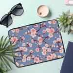 ]Infidu Elegant Cherry Blossom Floral Laptop Sleeve featuring pink cherry blossoms on branches with a soft blue background. the laptop sleeve on the table