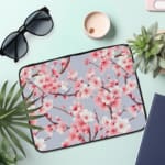 ]Infidu Elegant Cherry Blossom Floral Laptop Sleeve featuring pink cherry blossoms on branches with a soft blue background. the laptop sleeve on the table