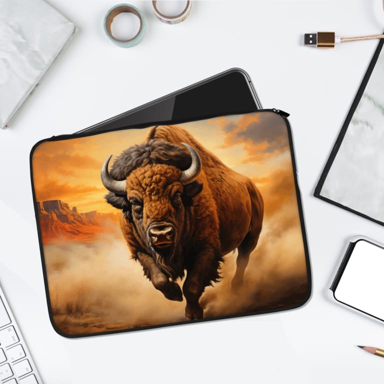 Laptop sleeve featuring a charging bison with brown fur in a warm desert landscape, made with durable fabric and a secure zip closure. laptop sleeve kept on a plain white background