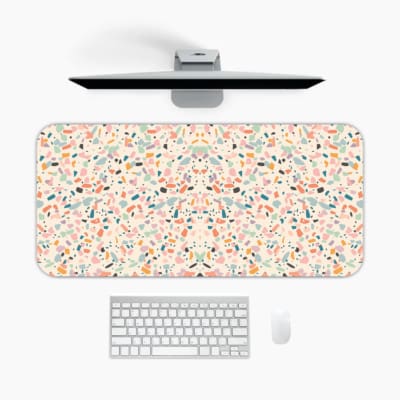 Infidu desk pad with a playful confetti pattern featuring small, colorful shapes on a light background. A desk pad under the computer