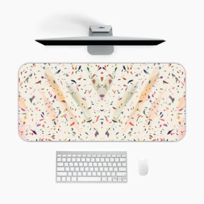 Infidu desk pad featuring a colorful terrazzo pattern with scattered shapes in blue, pink, orange, and purple on a light background. A desk pad under the computer