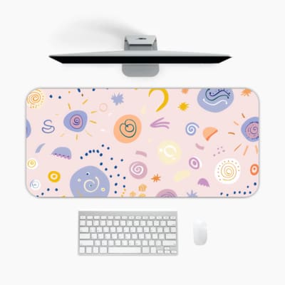 Infidu Playful Desk Pad featuring a light pink background with various small, colorful abstract shapes, spirals, and dots. A desk pad under the computer