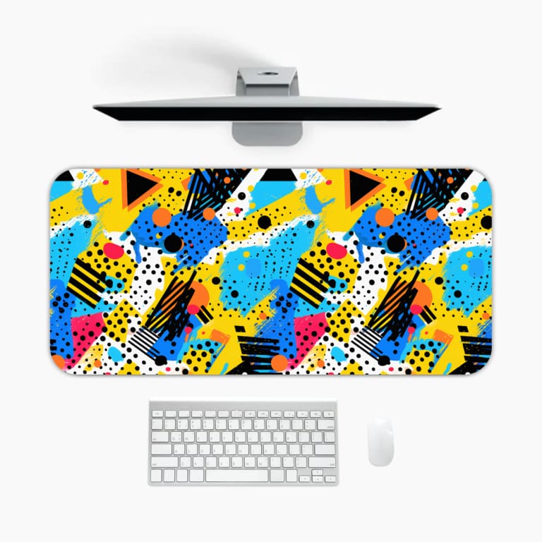 Infidu Colorful Abstract Desk Pad featuring playful geometric shapes in yellow, blue, pink, black, and turquoise on a white background. A desk pad under the computer