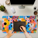 Infidu vibrant geometric desk pad with colorful abstract shapes and yellow background A computer and laptop are next to the desk pad