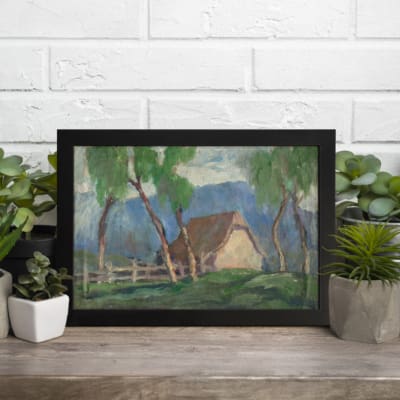 Vintage wall art of a countryside cottage with green trees and soft blue mountains. displayed on the wall