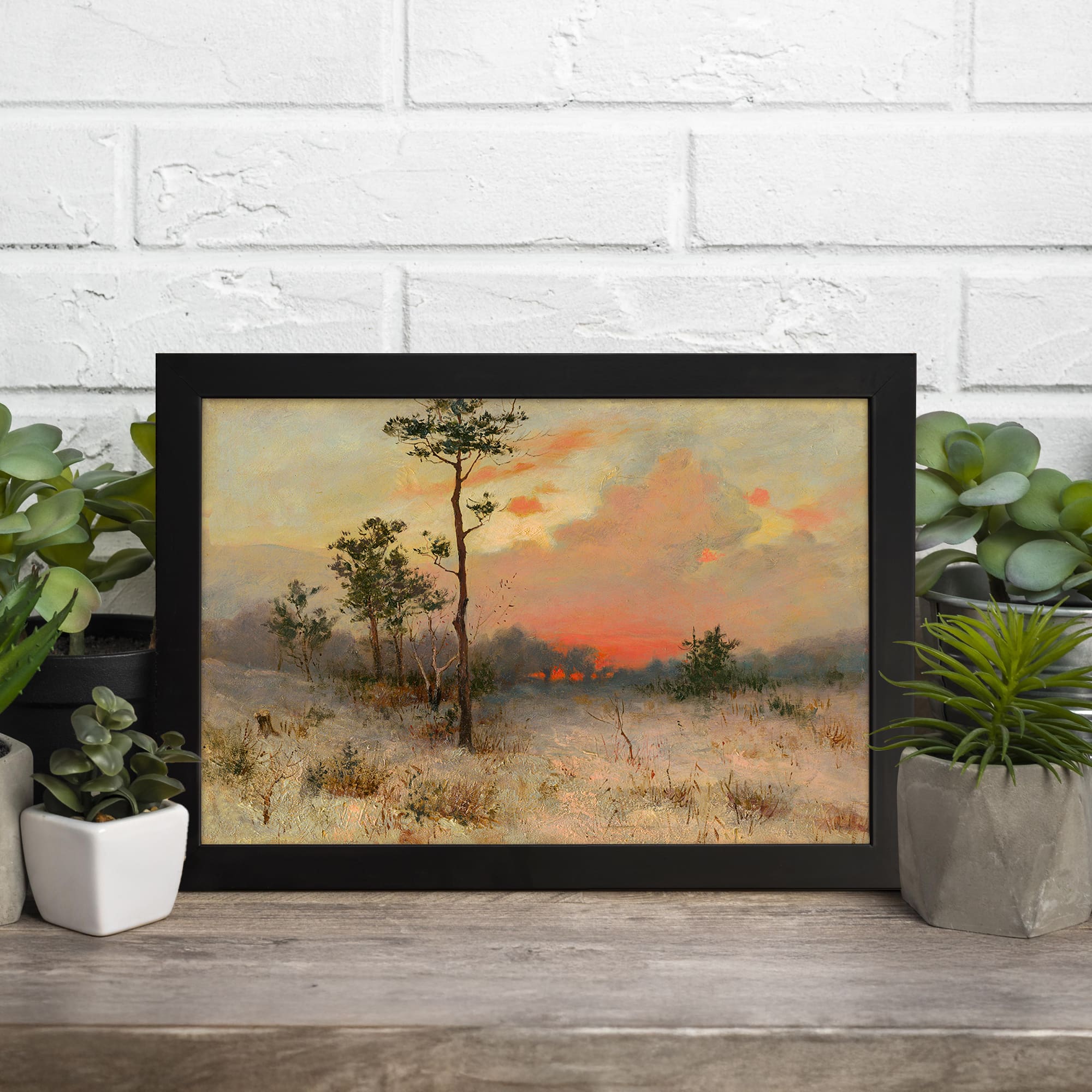 Vintage winter landscape wall art featuring a snow-covered field, sparse trees, and a serene sky with soft pink, orange, and blue tones. hung on the wall in a black frame