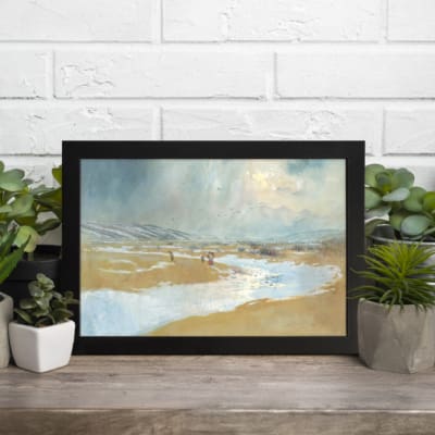 Vintage coastal landscape wall art with soft blue skies and beige terrain, perfect for adding a calm and serene vintage touch to any room. displayed on the table in a black frame
