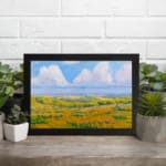 Infidu vintage wall art featuring a serene pastoral landscape with rolling hills, open fields, and soft clouds in the sky. displayed on the wall art in a black frame