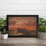 Vintage wall art of a wooden ship at sunset with fiery red, orange, and pink sky, calm sea, and small human figures near the shore. displayed on the wall