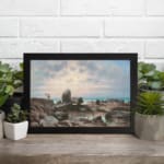 Vintage wall art of a rocky coast with calm blue water and a soft pastel sky in pink, cream, and blue tones. displayed on the wall