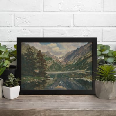 Vintage wall art depicting a serene mountain lakeside scene with reflection in the water, featuring natural greens, blues, and earthy tones. displayed on the table in a black frame
