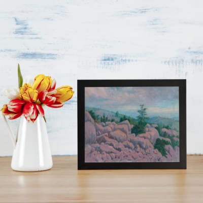 Vintage wall art featuring a serene rocky landscape with pastel colors, soft blue sky, and natural, calming tones. displayed on the table in a black frame
