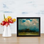Vintage cloudscape wall art with soft pink, gray, and white clouds over a calm green landscape. displayed on the wall