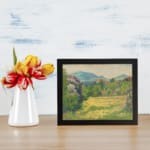 Vintage wall art featuring peaceful green fields, yellow flowers, and blue hills, creating a calming nature scene. displayed on the wall