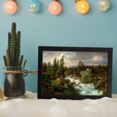Vintage river flowing through a dense forest, with green trees and soft blue sky, framed in black. displayed on the wall