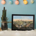 Infidu Classic Townscape with Rolling Hills Vintage Wall Art featuring a peaceful town view with green hills, a river, and church towers. displayed on the wall