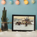 Vintage wall art of a snowy village with people at a small market, surrounded by wooden houses and a cloudy sky. displayed on the wall