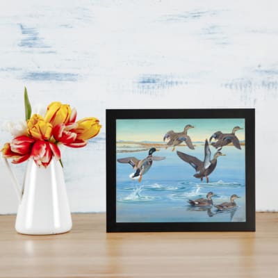 Infidu Vintage Wall Art featuring ducks flying and floating on calm water with soft colors and serene background. displayed on the table in a black frame