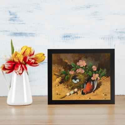 Vintage wall art depicting a bird nest with pink flowers and eggs, creating a rustic, nature-inspired aesthetic. displayed on the table in a black frame