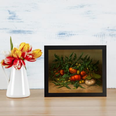 Vintage wall art of a vibrant vegetable still life featuring tomatoes, greens, and earthy tones with a warm, rustic background. displayed on the table in a black frame