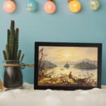 Vintage wall art of a fisherman by a calm lake at sunset with golden sky and soft reflections. displayed on the wall