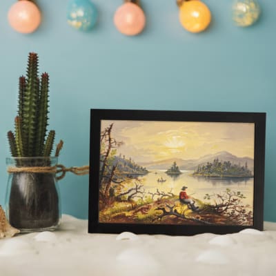 Vintage wall art of a fisherman by a calm lake at sunset with golden sky and soft reflections. displayed on the wall