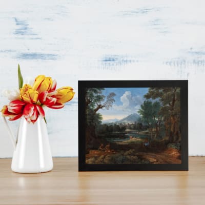 Vintage wall art featuring a serene countryside landscape with trees, mountains, and a peaceful path. Ideal for home decor. displayed on the table in a black frame