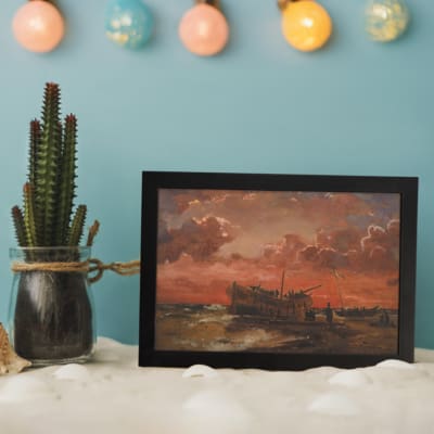 Vintage wall art of a wooden ship at sunset with fiery red, orange, and pink sky, calm sea, and small human figures near the shore. displayed on the wall