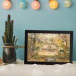 Vintage wall art of a peaceful countryside with a stream, tall trees, and a wooden house in soft earthy tones. displayed on the wall