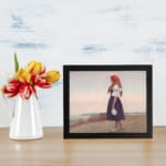 Vintage wall art of a woman on a grassy cliff overlooking the sea, wearing a red headscarf and holding a jug, in soft earthy tones. displayed on the wall