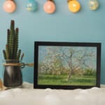Vintage wall art of a spring meadow with a blossoming tree in soft pink, green, and blue tones by Infidu. displayed on the wall