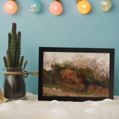 Vintage wall art featuring earthy bushes and trees in warm browns and greens, framed in black with a soft, muted background. displayed on the table in a black frame