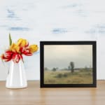Infidu vintage wall art of a quiet countryside with soft green fields, trees, and a cloudy sky in muted tones. displayed on the wall